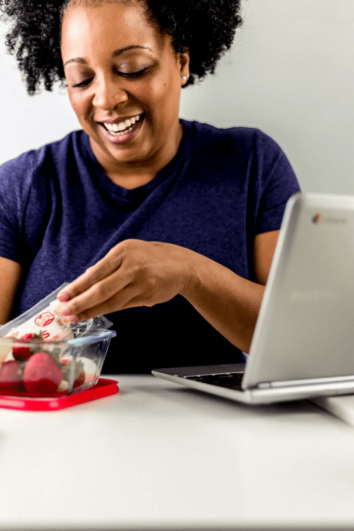 woman smiling sitting at table with laptop and strawberries