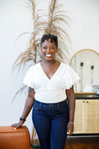 woman smiling and standing in a room wearing jeans and a white top