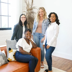 4 women sitting on a couch or standing near it