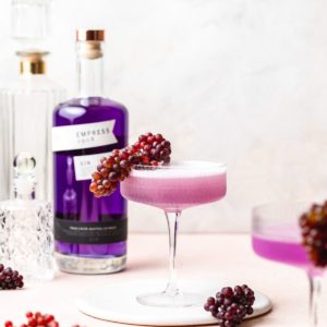 a coup glass filled with a purple cocktail and topped with tiny grapes