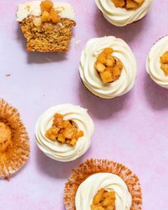cupcakes on a pink surface topped with cut up fruit and white icing