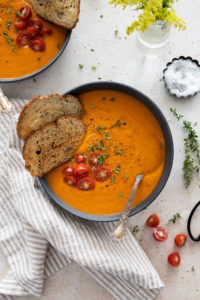 tomato soup in a bowl with two pieces of bread and toppings
