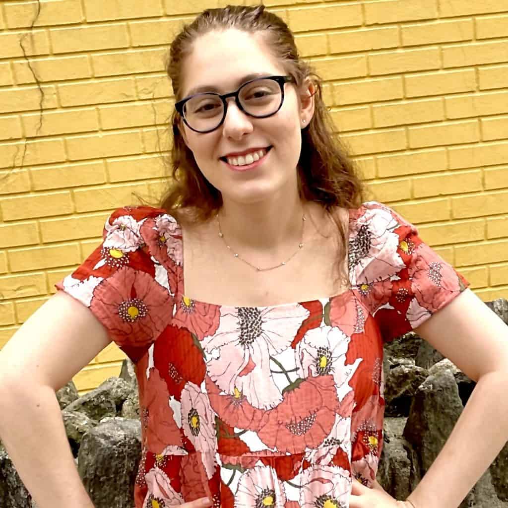 woman smiling in glasses in front of a yellow brick wall