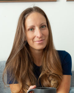 woman in a blue shirt with brown hair smiling and holding a grey coffee mug