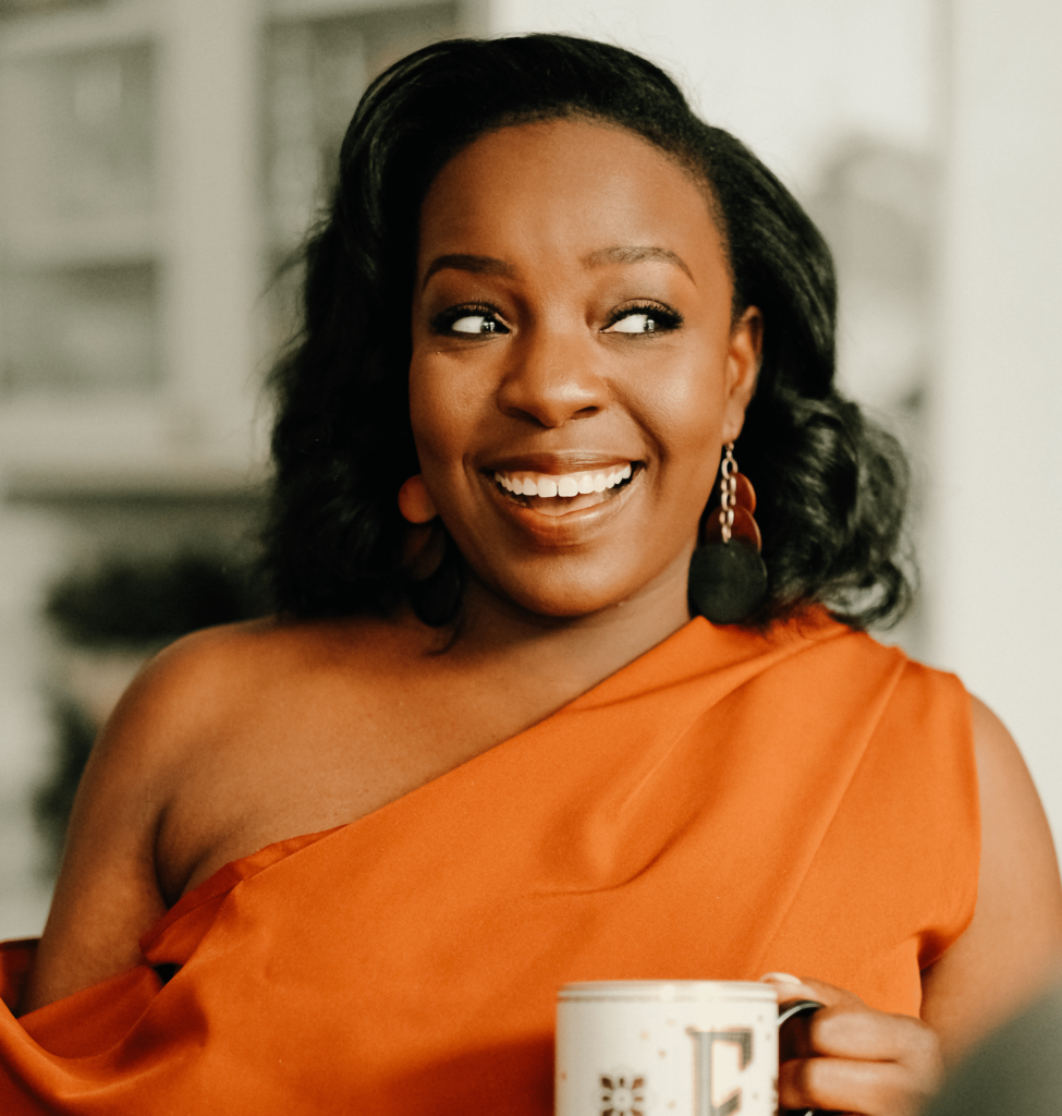 woman in an orange top holding a mug and smiling