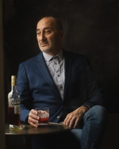 man in a blue suit holding a glass and a bottle of liquor