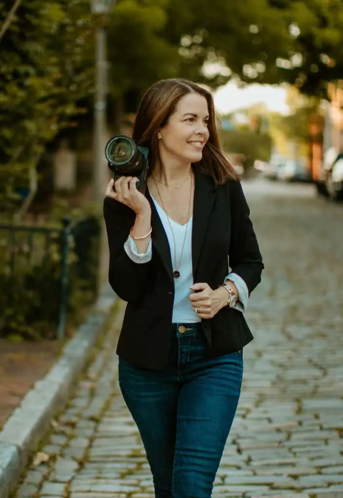 woman in a blazer and jeans standing on a street with a camera