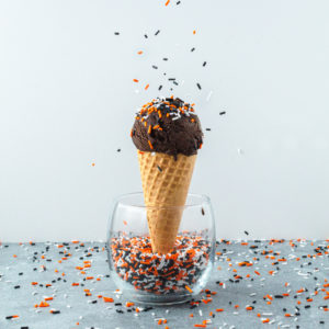 scoop of ice cream in a cone in sprinkles in a cup with more sprinkles poured on top