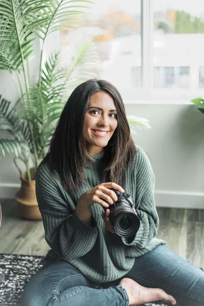 woman sitting on the ground in a green sweater holding a camera