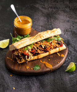 sandwich open on a wooden board with a jar of sauce