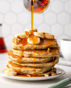 pancakes stacked and topped with bananas and syrups pouring on