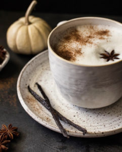 latte in a mug with anise pod on top and pumpkin in background