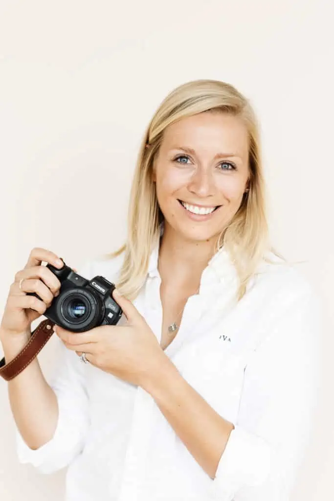 woman in white shirt with blond hair holding a camera and smiling