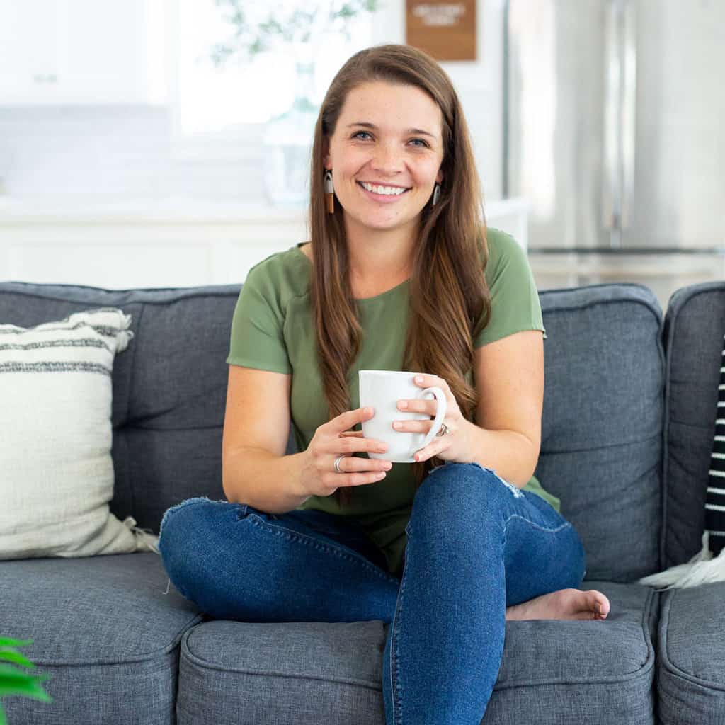 woman sitting on couch in jeans with a green shirt holding a mug and smiling