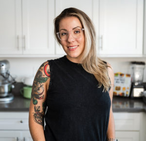 woman in a white kitchen and a black top smiling at the camera