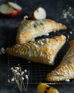 three apple hand pies with drizzles of white frosting on a rack and apple sliced in the back