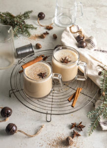 two cups of eggnog chai cocktails with cinnamon sticks on a rack