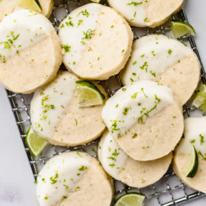 close up of nine key lime pie cookies with white frosting, lime zest, and slices of lime