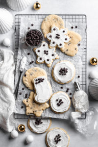 eleven frosted chocolate chip sugar cookies with white frosting and chocolate chips on a baking sheet and rack