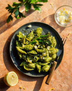 goddess green pasta on a black plate with a fork. half lemon and garnish in the background
