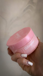 close up of someone with white nails holding a pink Glimmr hair treatment tube and water droplets