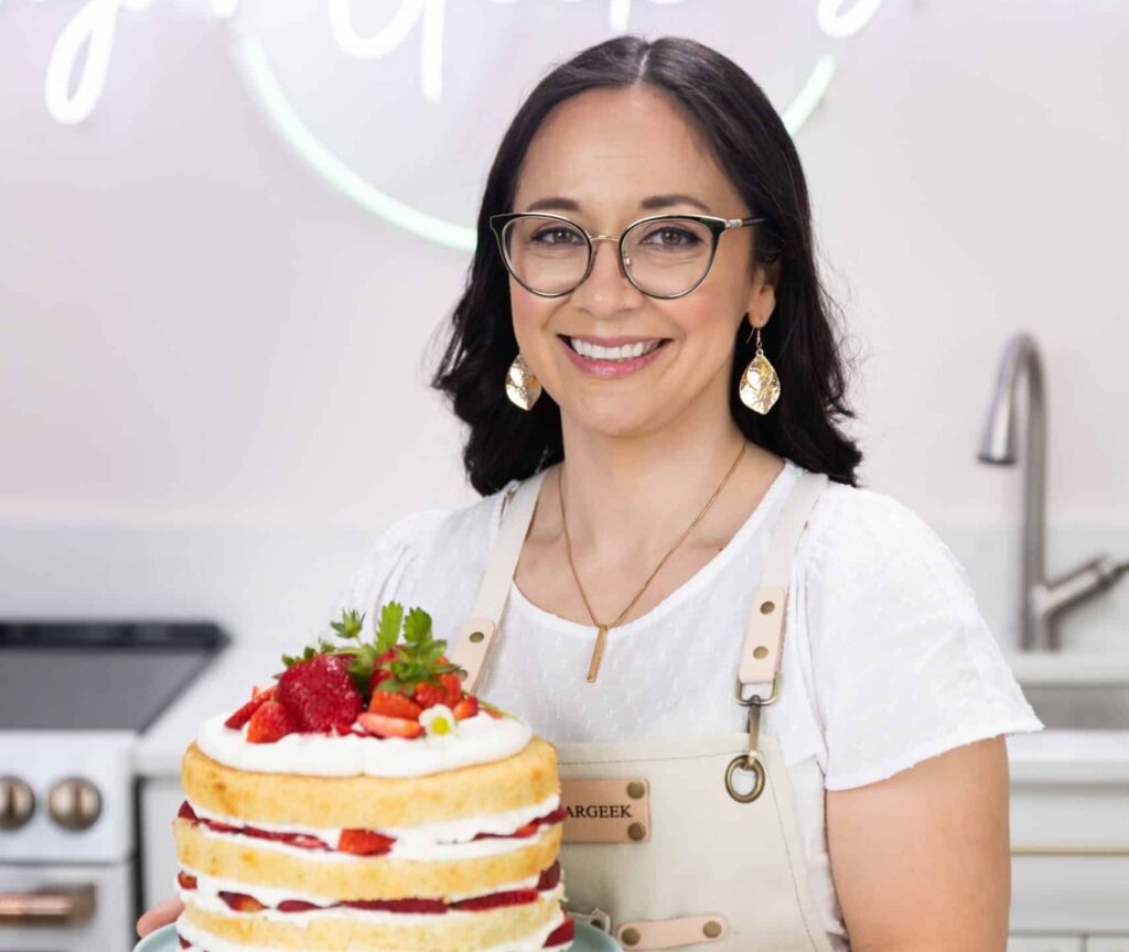 person in white shirt and apron holding a cake with strawberries