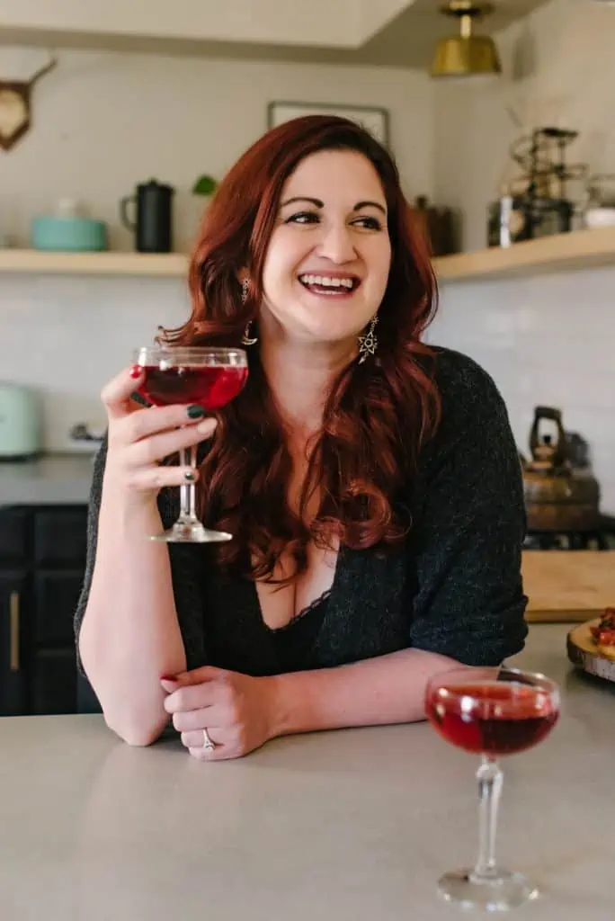 woman with red hair holding a wine glass with red wine and smiling