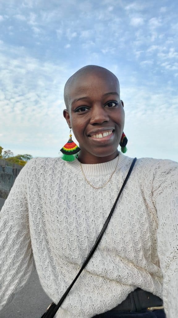 woman with a white sweater and red, yellow, blue and green earrings smiling outdoors
