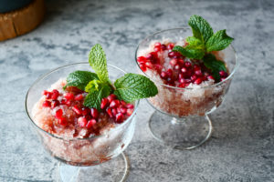 two cups of pomegranate shaved iced with pomegranate and garnish toppings