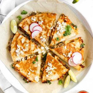 carne asada quesadilla cut with slices of radish, lime, and crumbles of cheese