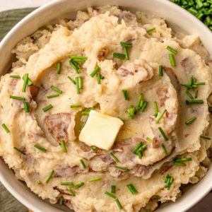 close up of garlic mashed potatoes in a bowl with toppings and butter