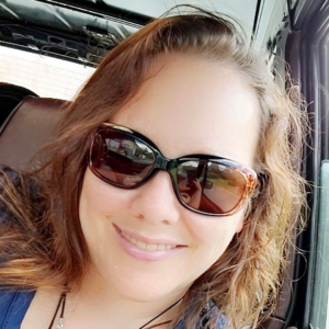 woman with brown hair and wearing sunglasses smiling