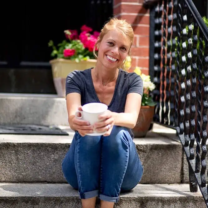 blonde woman sitting on steps with a white coffee mug and smiling