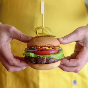 close up of a person in a yellow shirt holding a burger with toppings