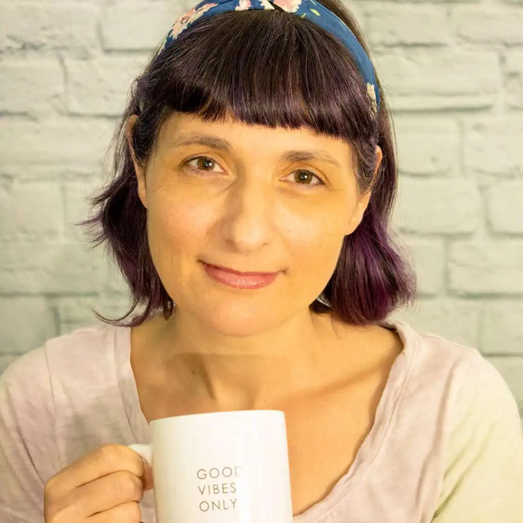 woman with short brown hair and bangs wearing a headband and holding a white mug