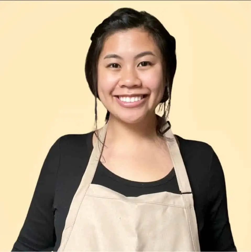 woman with dark hair wearing a black long sleeve and apron smiling
