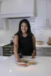 woman with dark hair wearing a black tank top fixing a plate and smiling to the camera