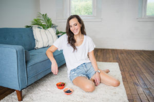 brunette woman wearing a white shirt leaning on a blue couch smiling