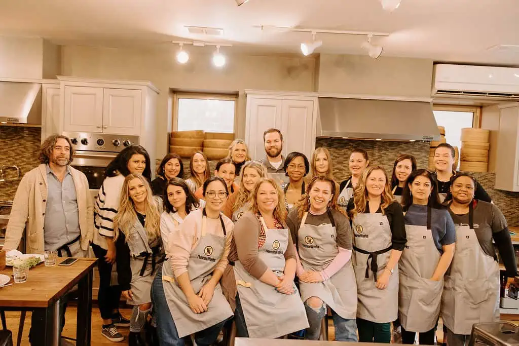 group of people in aprons standing in a kitchen and smiling at the camera