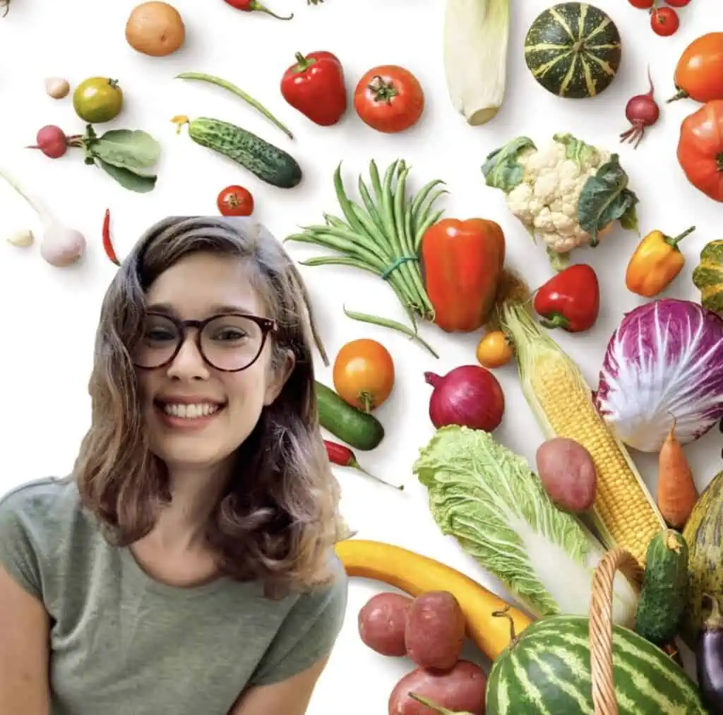woman with short brown hair wearing brown glasses and green shirt smiling in front of a vegetable background