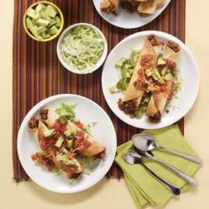 two white plates with two taquitos with toppings next two bowls of shredded lettuce and cut avocado