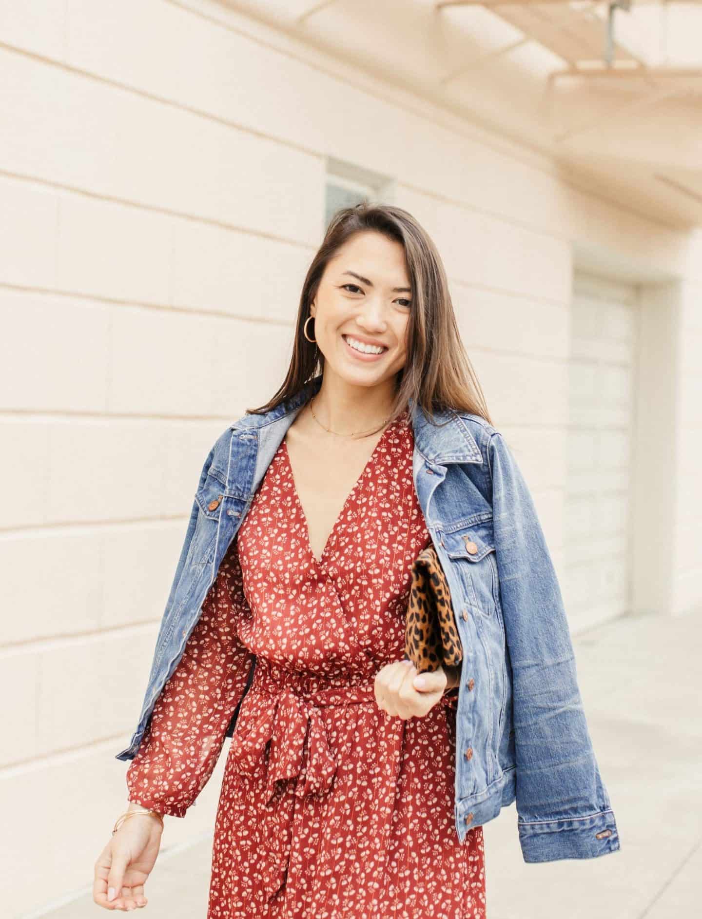 woman with brown hair wearing a red printed dress and jean jacket smiling to the camera