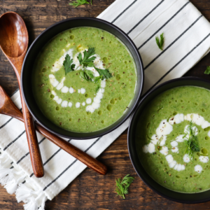 two bowls of green roasted garlic and watercress souple with lemon creme fraiche next to two wooden spoons and a stripe cloth