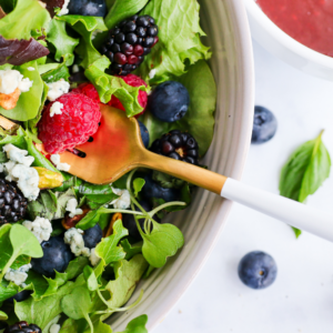 close up of a gold fork in bowl of salad with berries and different toppings