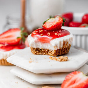 mini cheesecake on a stack of plates with white and red frosting and a slice of strawberry on top