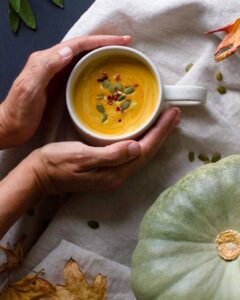 soup in a cup with hands and a pumpkin