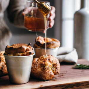 A woman's hands pour honey over buns on a wooden cutting board.