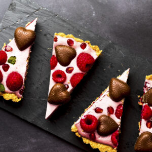 Triangular pie slices on a black background. Pink frosting with raspberries, pomegranates, and chocolate hearts.