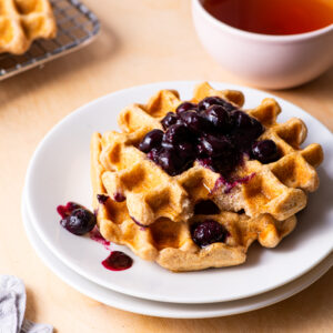 a white plate with a waffle on top. The waffle has a blueberry compote on top.