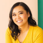 Lisa Childs smiling warmly, wearing a yellow top with pearl jewelry, against a soft peach and green background.
